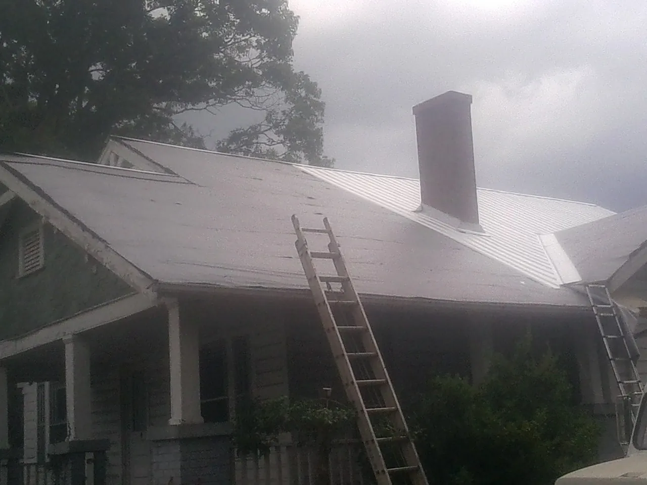 Ladders against a metal roof on an older home with a brick chimney in Almont