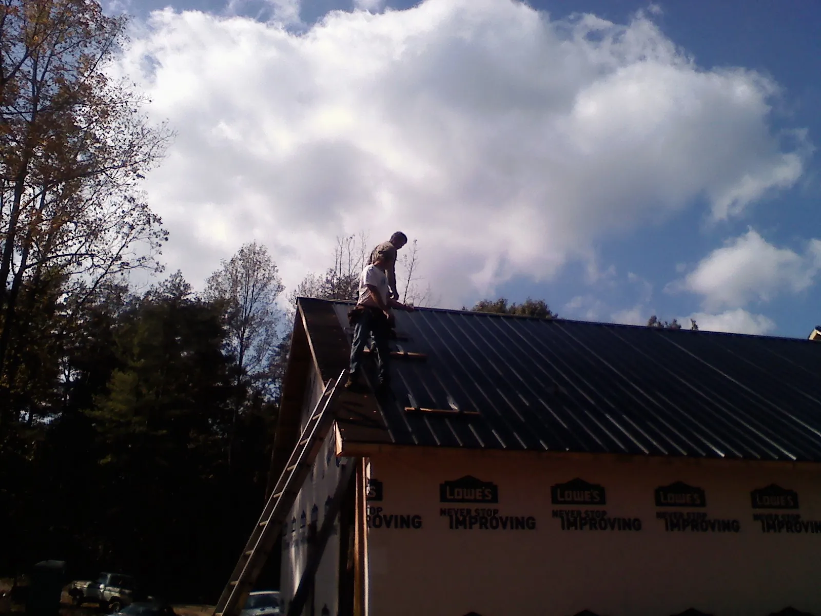 Roofer fastening dark metal panels high against a cloudy sky, from a Roof Inspection job in Almont